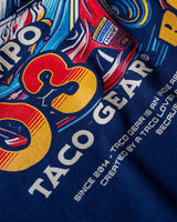 Taco Gear Al Pastor Racing t-shirt with colorful taco-themed racecar graphic, devil driver, and bold “Tacos de Trompo” and “Racing” text on navy and red tees.